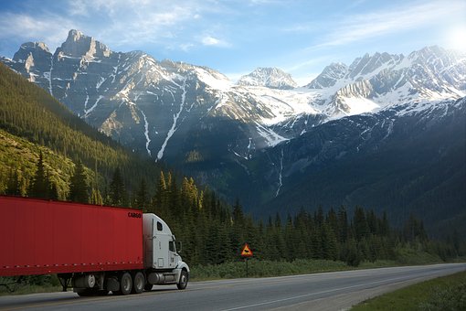 A semi truck drives down a highway with snowcapped mountains in the background