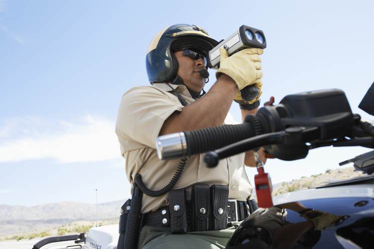 A police officer sits on a motorcycle and aims a radar detector at the road.
