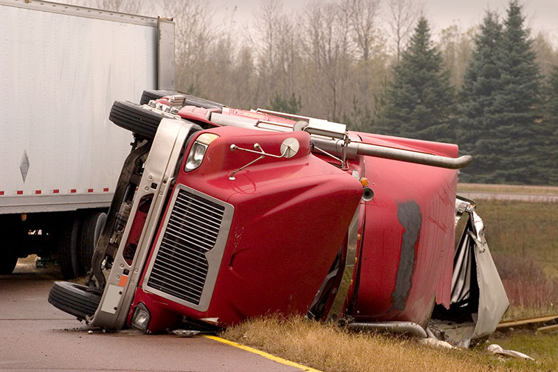 A red semi truck lays on its side in the middle of a highway after an accident.