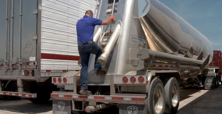 A worker steps on the back of a hazardous materials semi truck.
