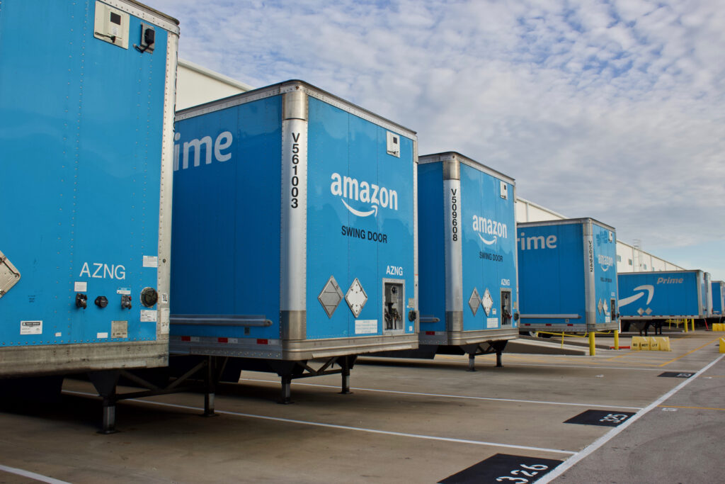 Several Amazon Prime semi trucks parked at loading docks behind a building