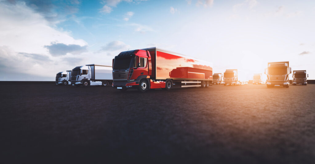 A fleet of semi trucks in a parking lot with the setting sun in the background