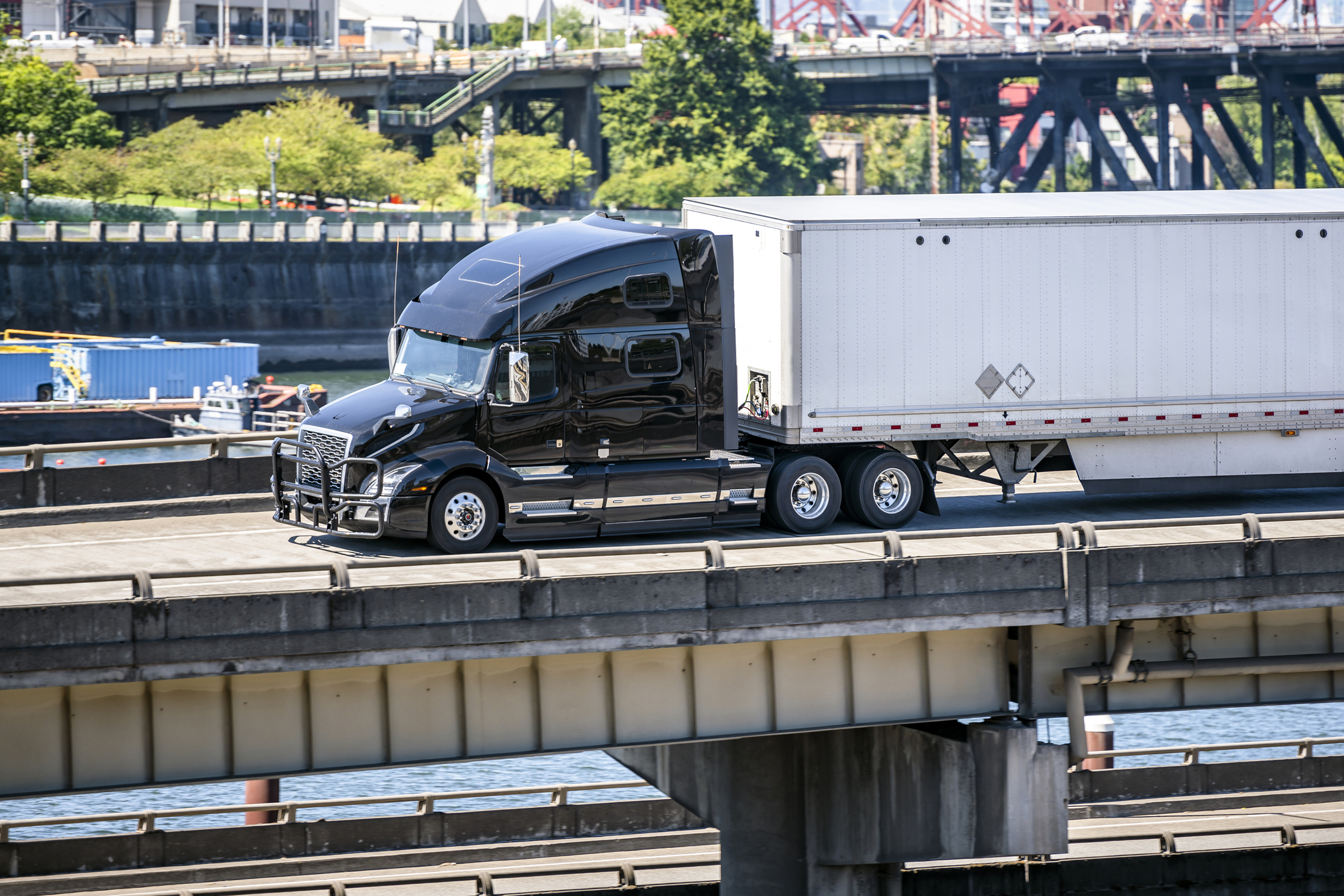 A black semi truck drives over a busy bridge.